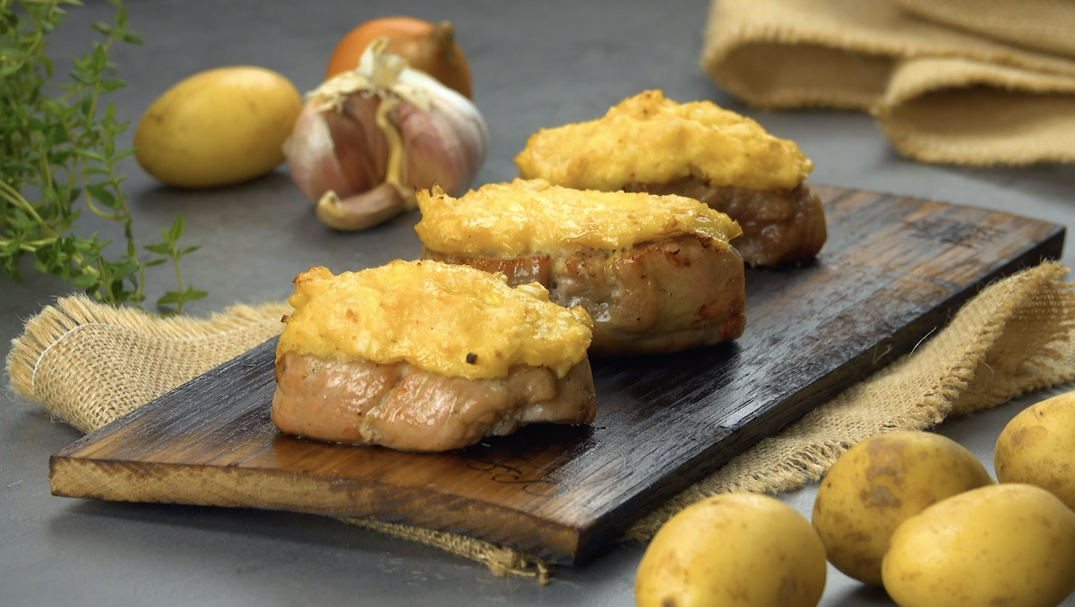 3 gegrillte Schweinefilets mit Frischkäse-Kartoffel-Kruste auf einem Holzbrett. Daneben Zutaten.