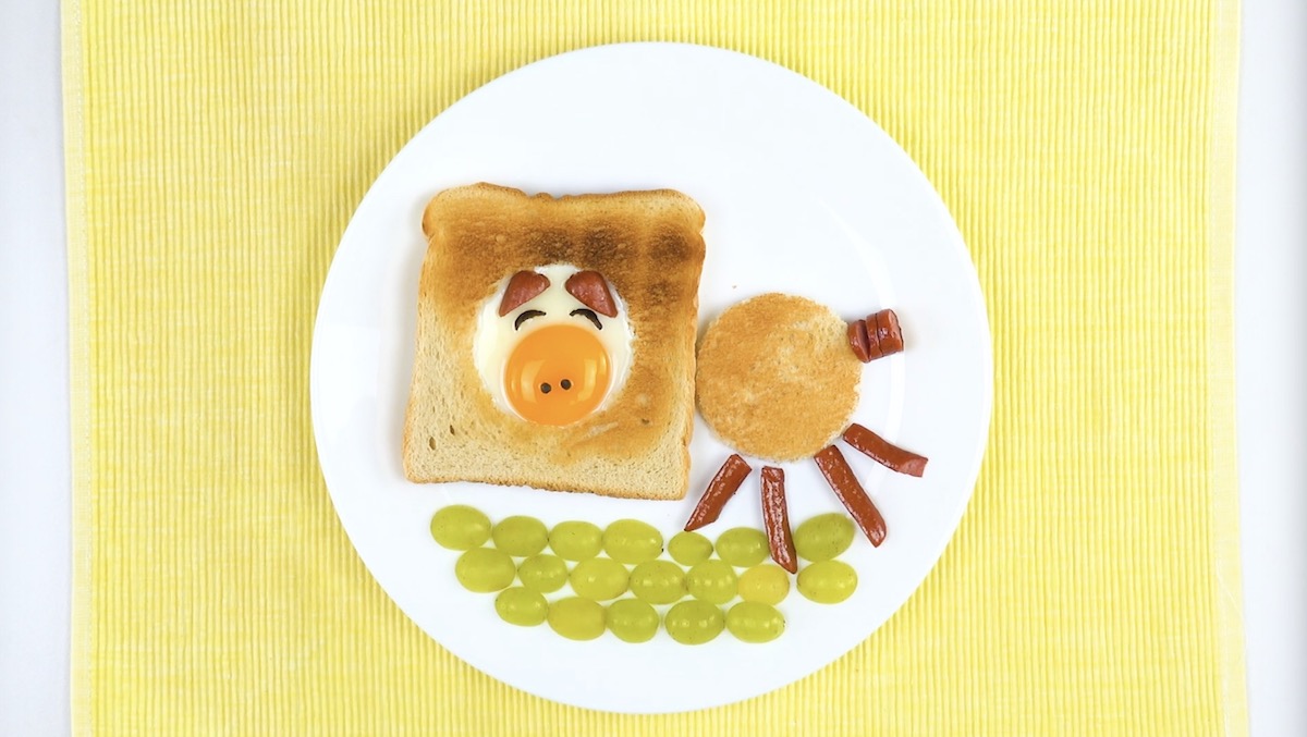 Toast-Schweinchen mit Ei, WÃ¼rstchen und halbierten Weintrauben auf Teller