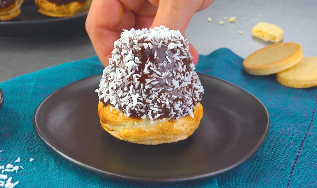 Blätterteig-Eclairs werden mit Kuvertüre und Kokosraspeln verziert