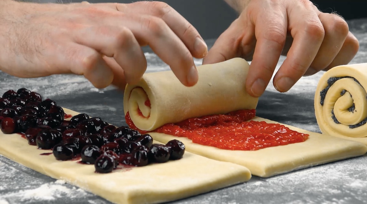 Die Teigstreifen des Croissant-Brots werden mit unterschiedlichen FÃ¼llungen bestrichen und eingerollt.