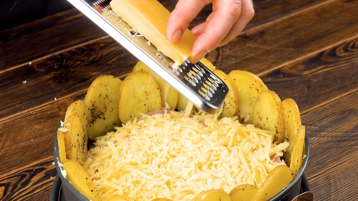Käse wird über Kartoffelscheiben in einer Springform gerieben.