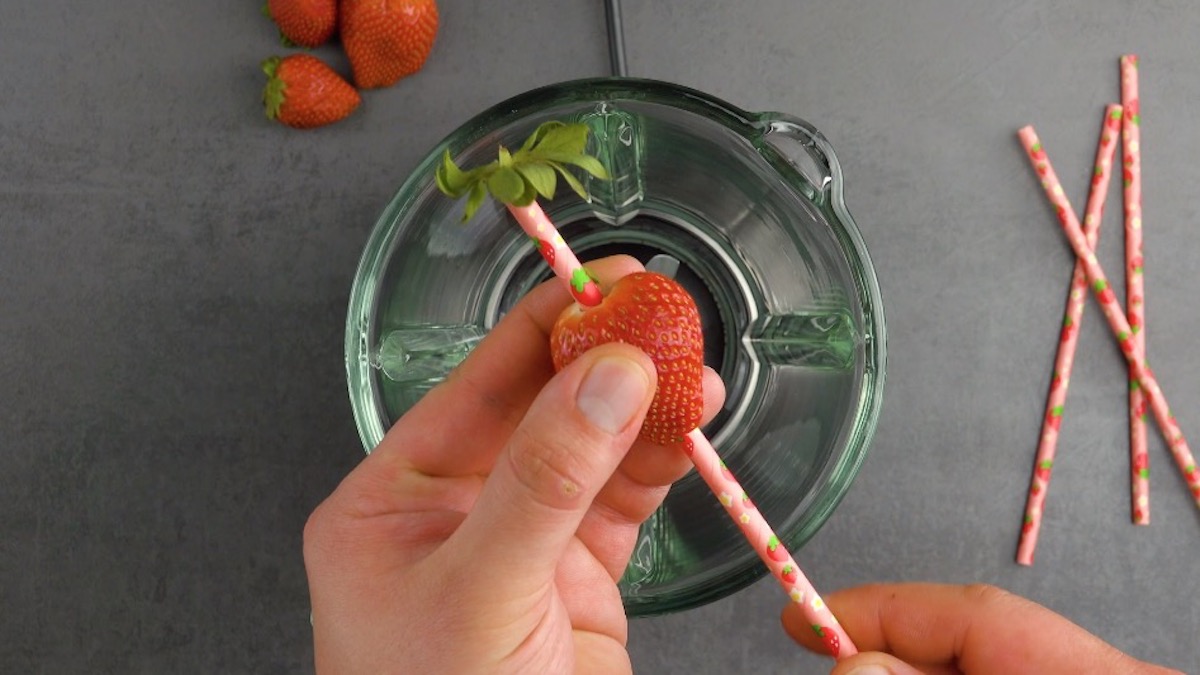 Der Strunk einer Erdbeere wird mithilfe eines Strohhalms entfernt
