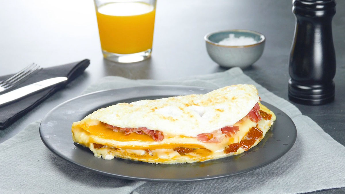 Ein geschichtetes Omelett auf einem grauen Teller. Im Hintergrund stehen Pfeffer, Salz und ein Glas Orangensaft.