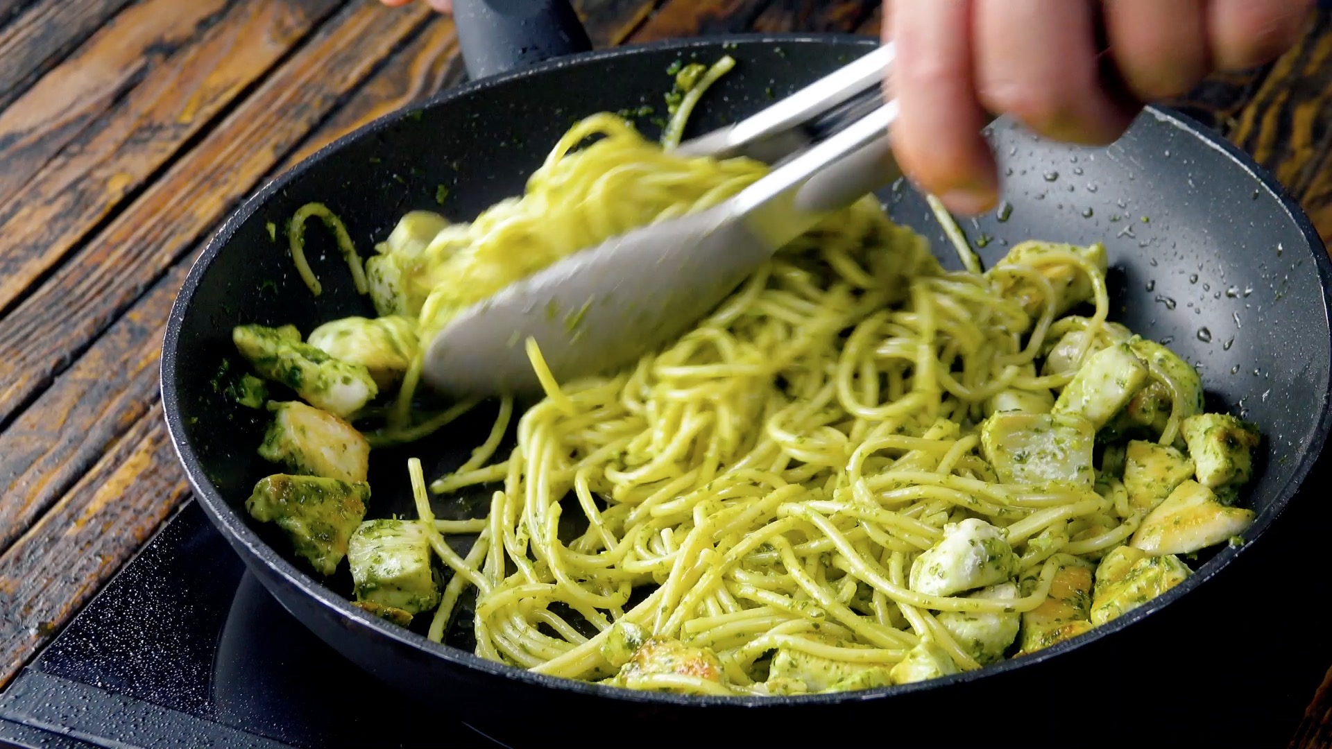 Gebratenes HÃ¤hnchen wird mit Pesto und Spaghetti in Pfanne vermengt