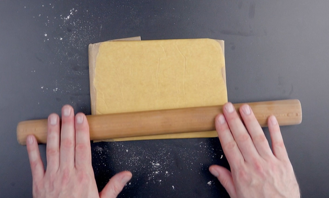 In Backpapier eingewickelte Butter wird mit Nudelholz zu Rechteck gewalzt