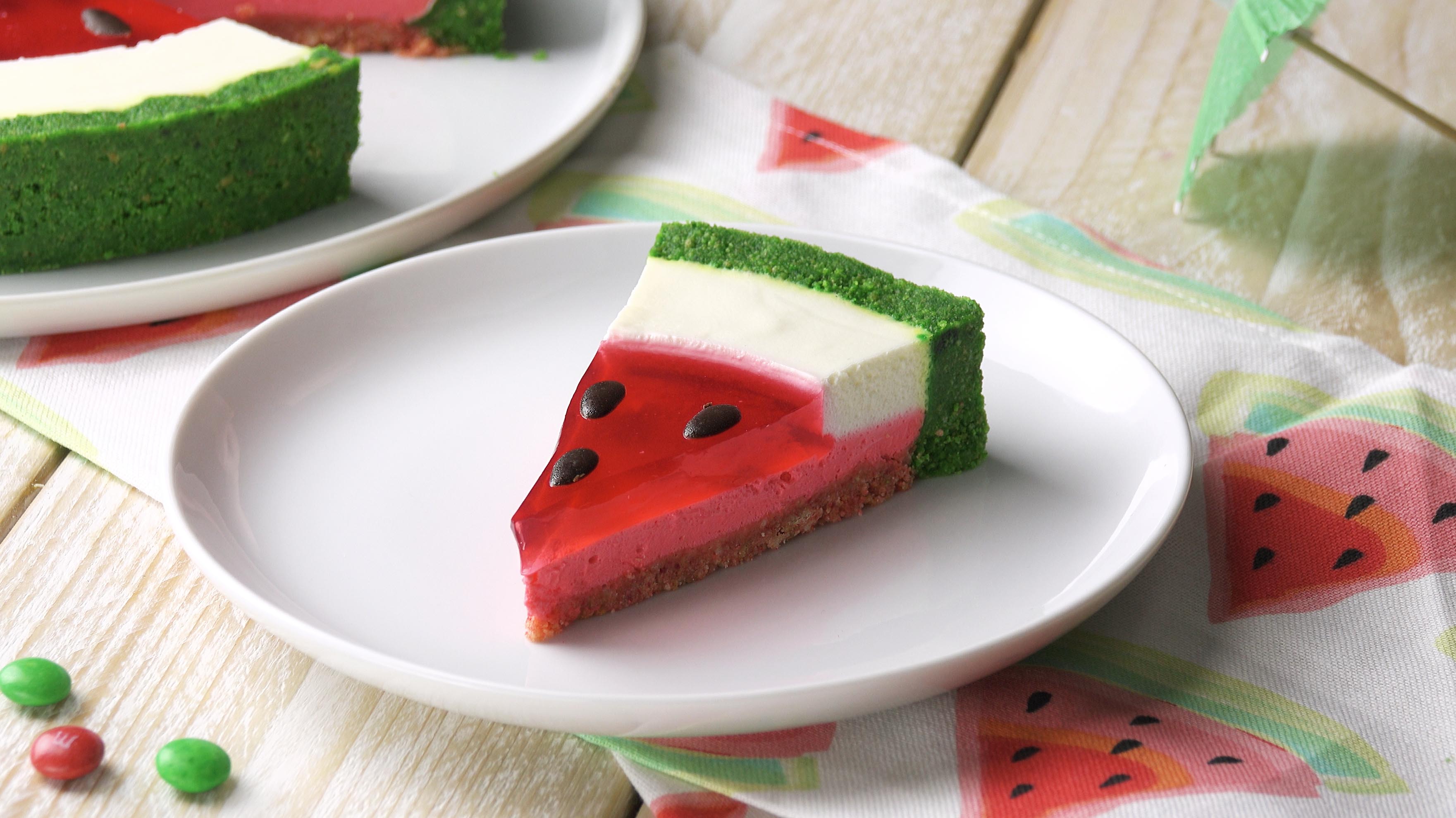 Ein StÃ¼ck Wassermelonen-Torte auf einem Teller mit der Torte im Hintergrund