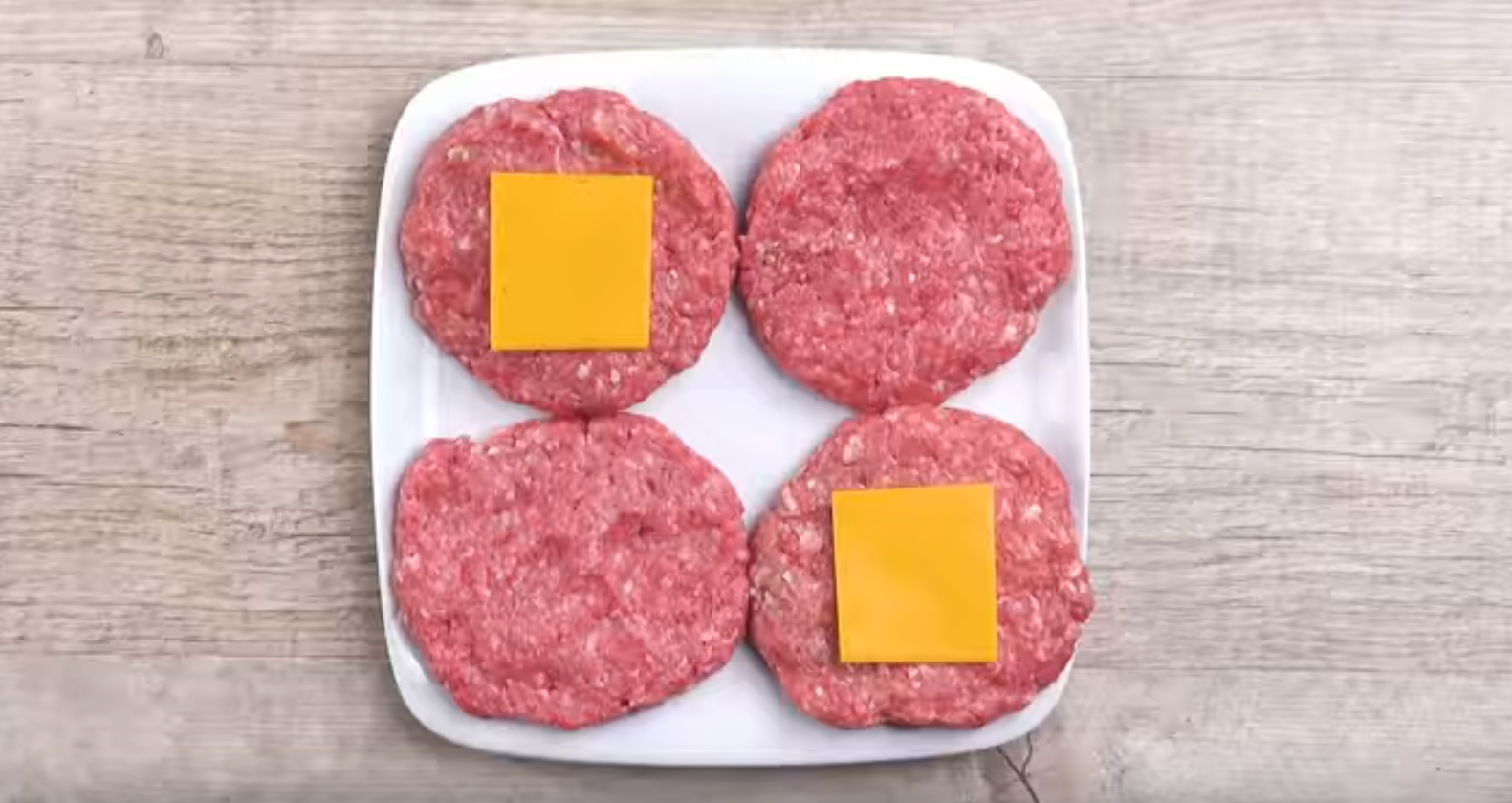 4 Burger-Pattys werden auf Teller gelegt und 2 davon mit eine Scheibe KÃ¤se belegt