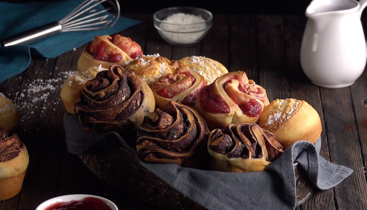 Unterschiedliche Cruffins in einem Brotkorb. Im Hintergrund Backzutaten. 