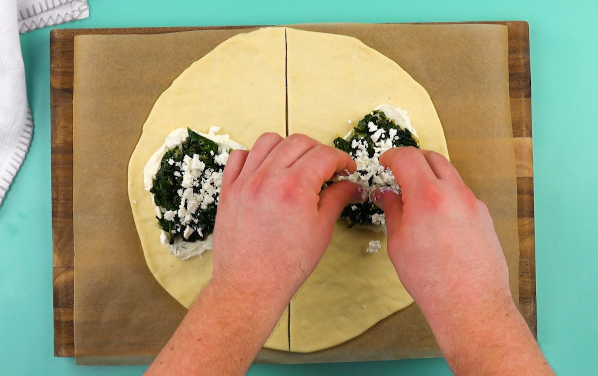 Feta wird Ã¼ber Spinat auf Pizzateig zerbrÃ¶selt.