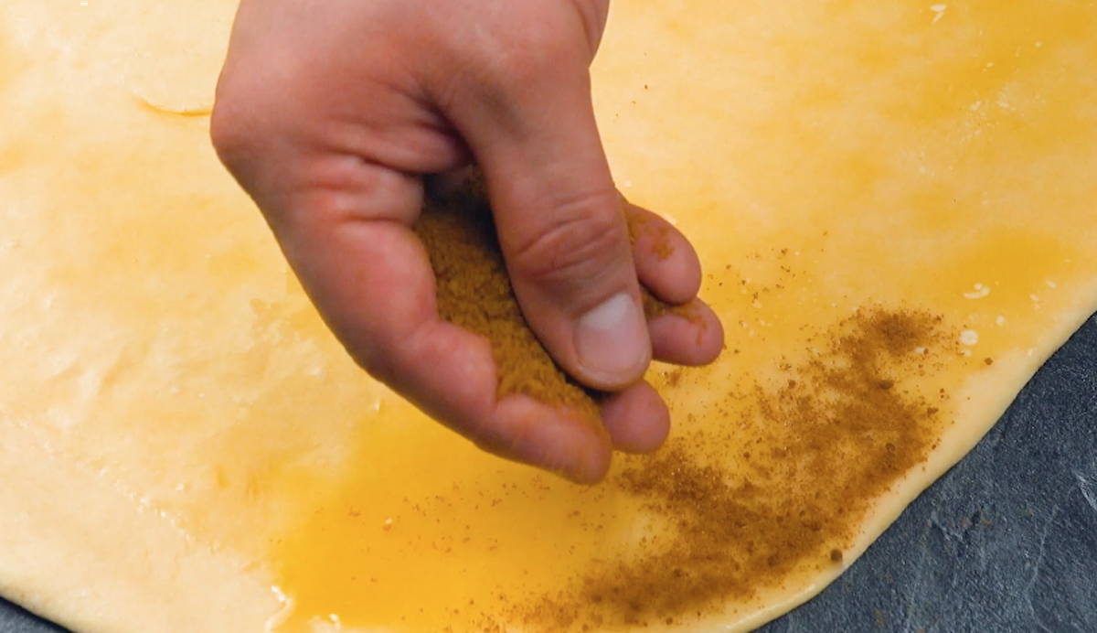 Mischung aus braunem Zucker, Zimt und Muskatnuss wird auf ausgerolltem Teig verteilt