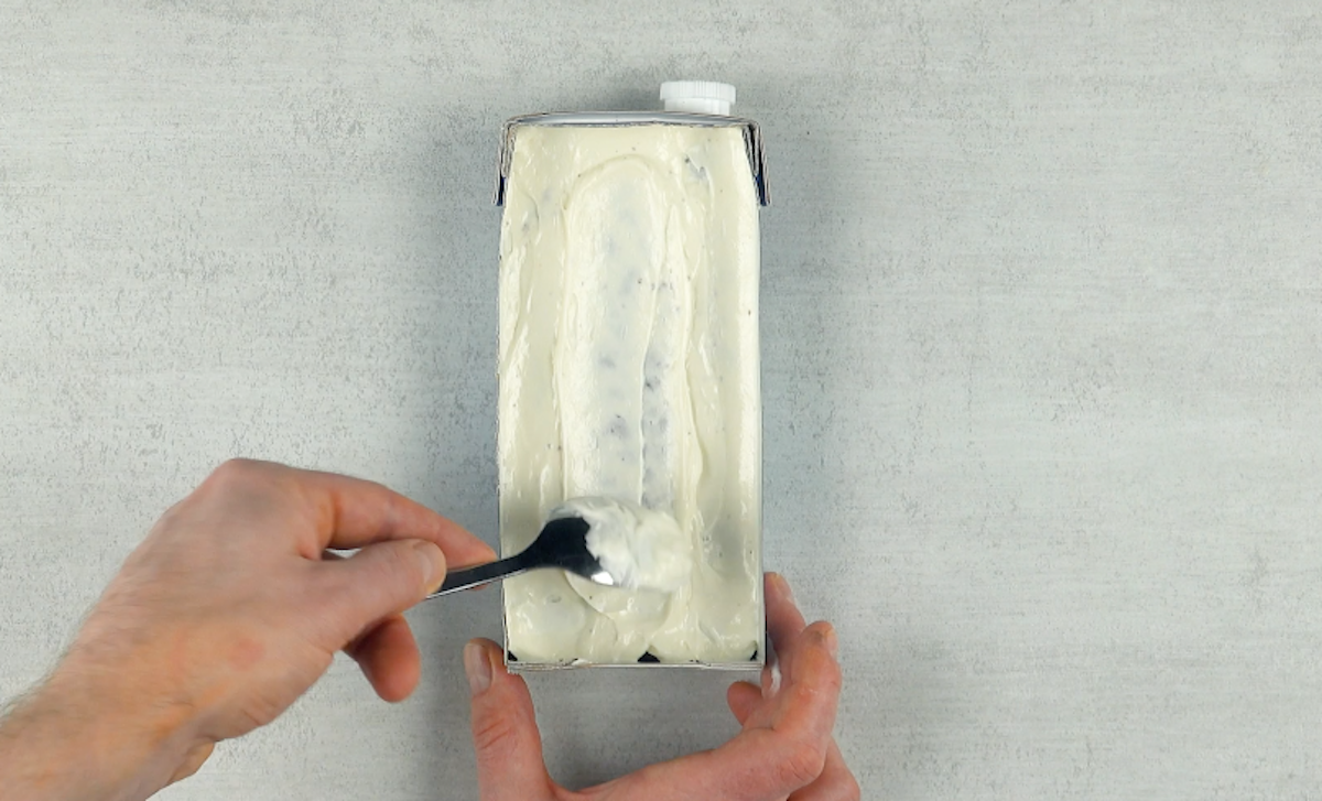 WeiÃŸe Creme wird auf Brownieboden in Milchkarton verteilt
