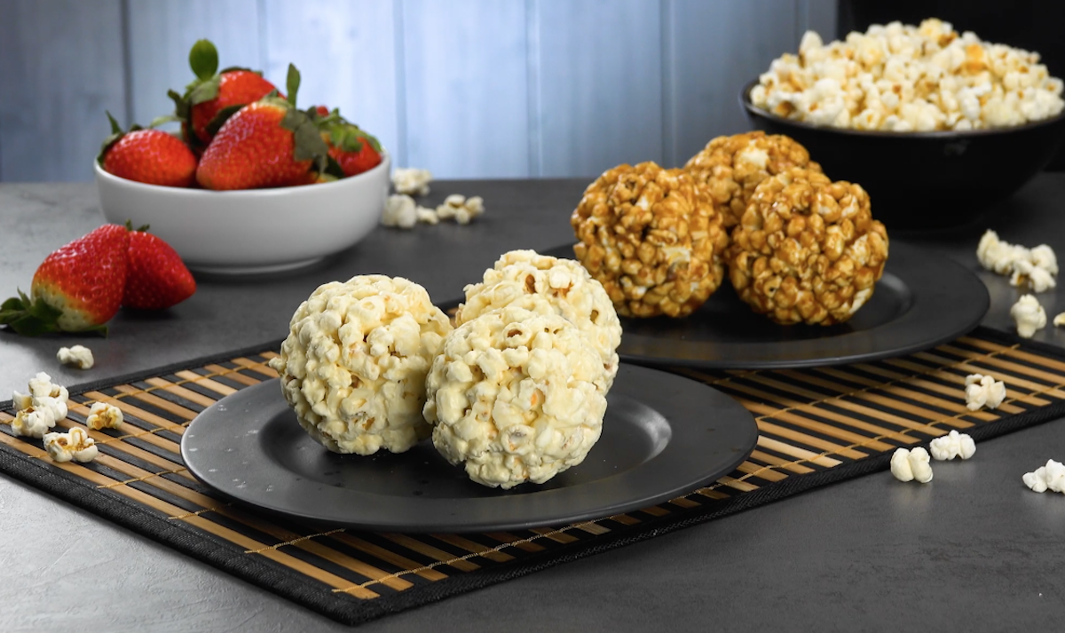 Zweierlei Popcorn-Bälle auf zwei Tellern, daneben eine Schale mit Erdbeeren und eine mit Popcorn