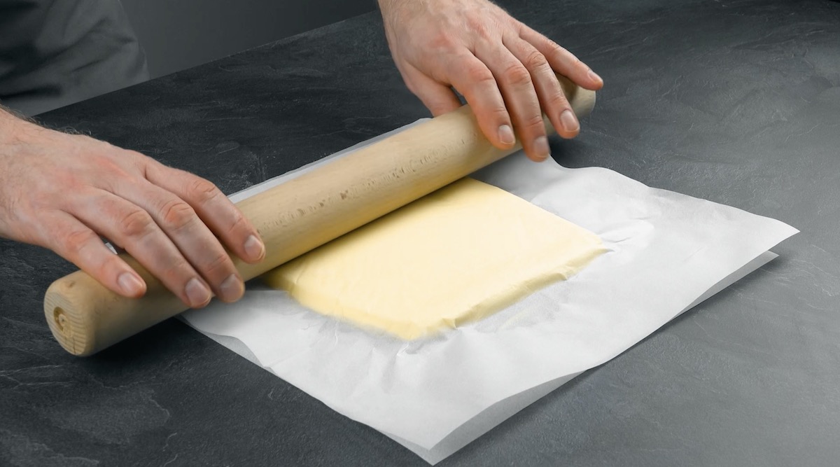 Butter wird zwischen Backpapier ausgerollt.