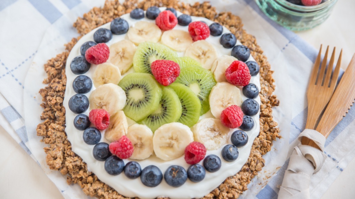 Frühstückspizza aus Haferflocken mit Joghurt und frischem Obst. Daneben liegt Besteck.