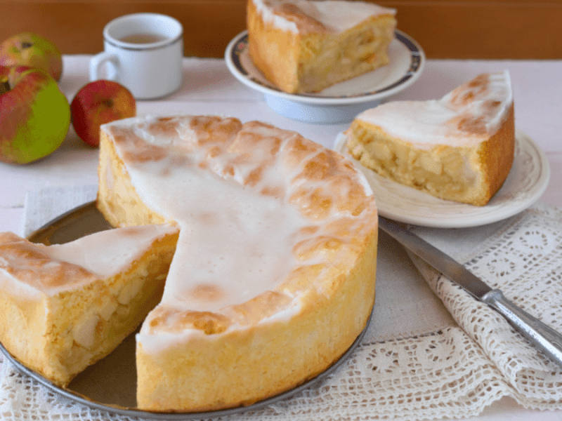 Ein gedeckter Apfelkuchen, aus dem mehrere Stücke entnommen wurden, daneben eine Tasse Kaffee und die Stücke auf Tellern
