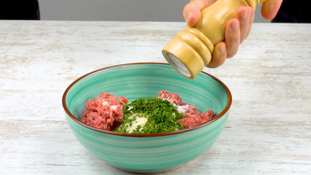 Hackfleisch wird mit Kräutern, Zwiebeln und Semmelbröseln in Schüssel gegeben und gewürzt