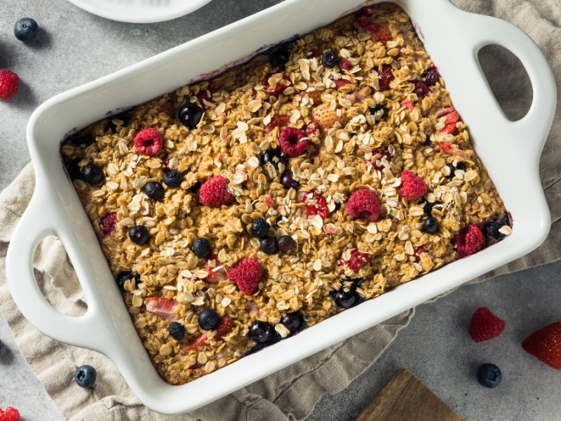 Ein Haferflocken-Auflauf mit Beeren von oben fotografiert. Daneben liegen Beeren und weitere Zutaten.