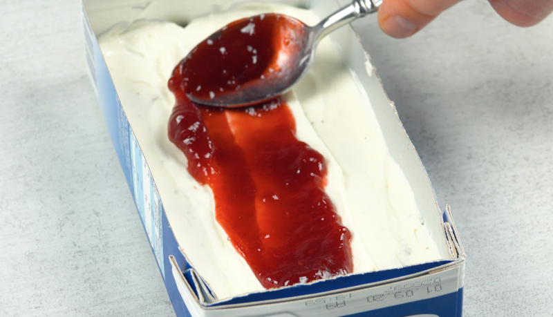 Marmelade wird mit LÃ¶ffel auf Creme in Milchkarton verteilt
