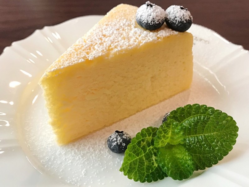 Ein Stück Joghurt-Kuchen mit Blaubeeren und Puderzucker auf Teller.
