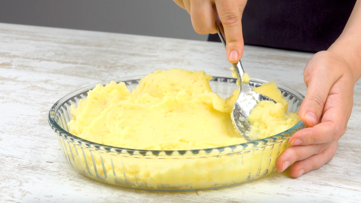 Kartoffelbrei wird mit Löffel in Auflaufform verteilt