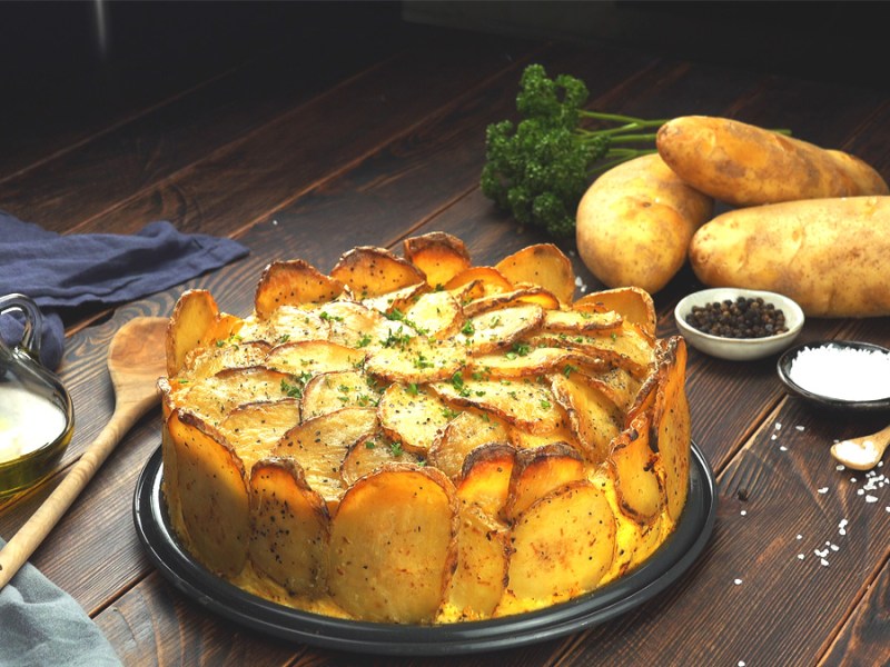 Ein Kartoffelkuchen, neben dem Zutaten und Schälchen mit Peffer und Salz sind.