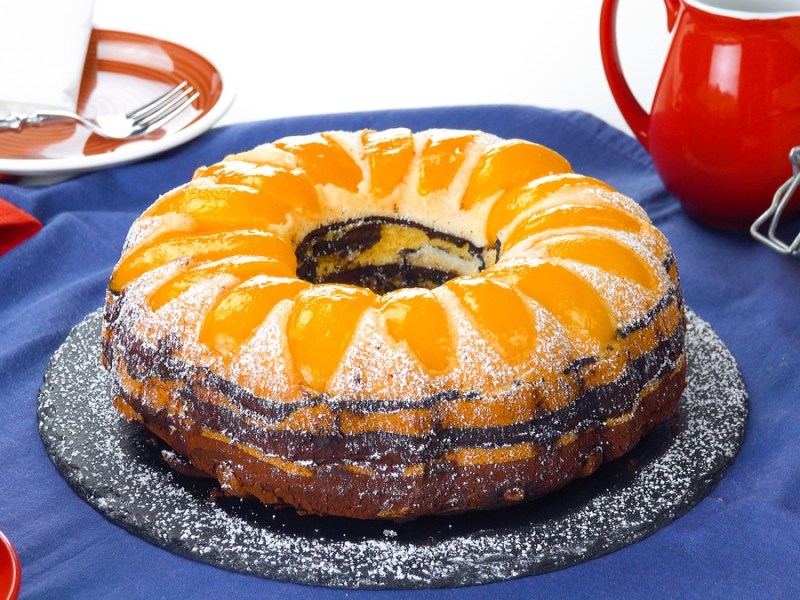 Pfirischkuchen mit Kakao im Wellenmuster auf einer Kuchenplatte.