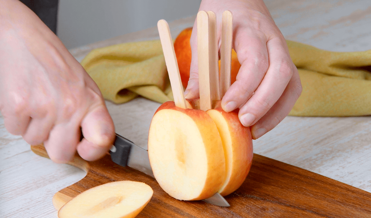 Ein mit Eisstielen bestÃ¼ckter Apfel wird in Scheiben geschnitten.