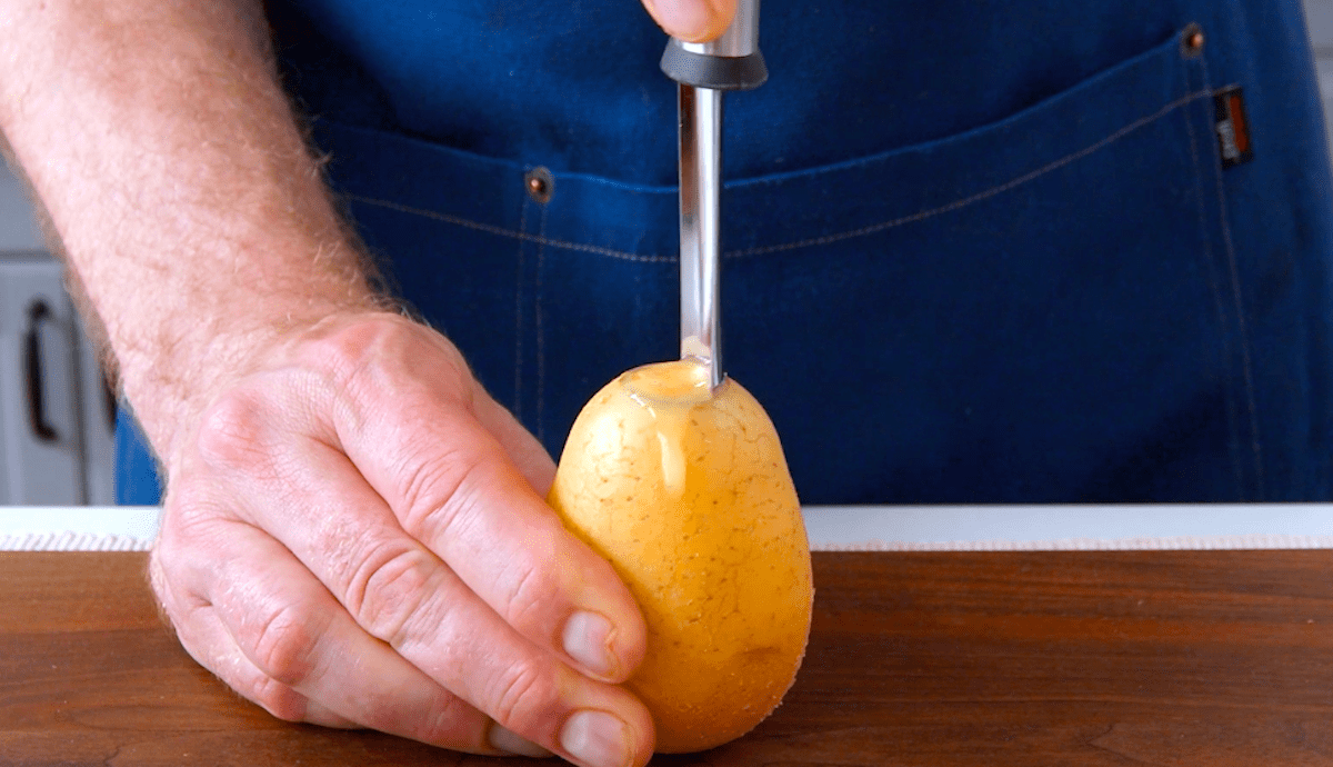 Ein Apfelausstecher wird in eine rohe Kartoffel gesteckt