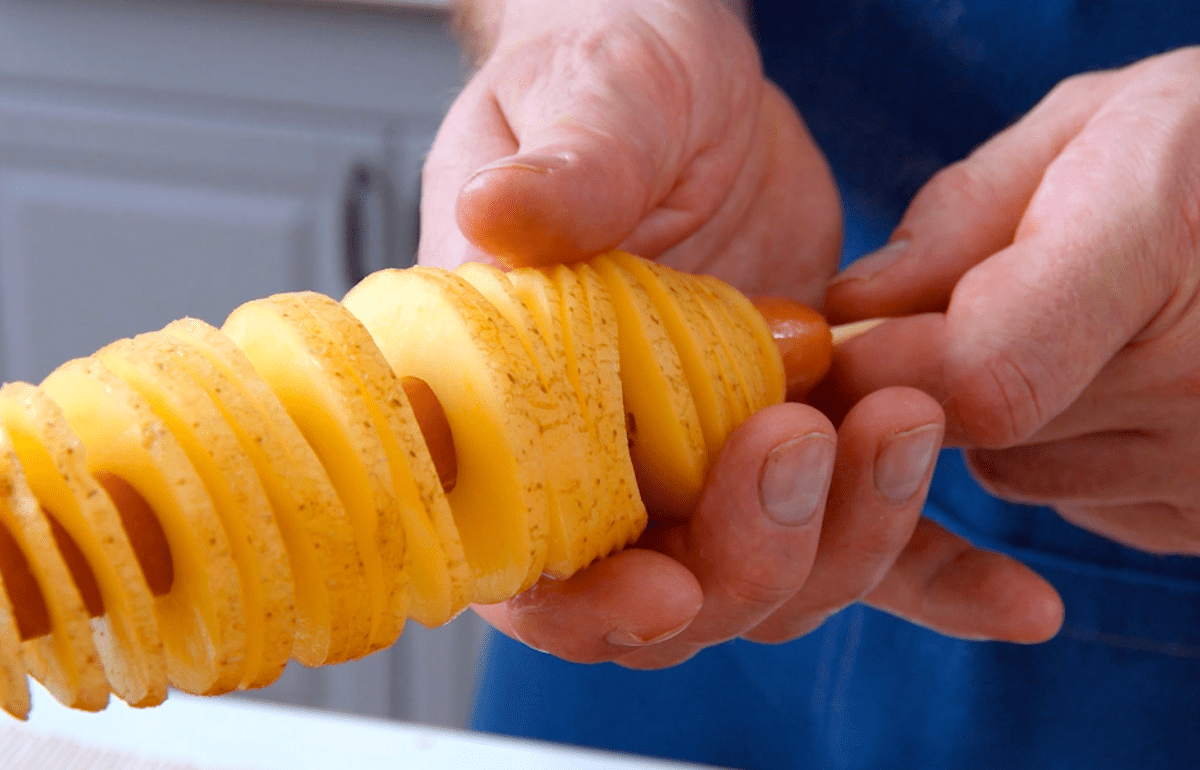 Eine Kartoffel wurde spiralartig eingeschnitten und wird nun rund um eine Wurst gezogen