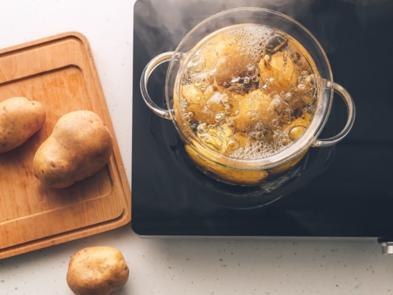 Salzkartoffeln kochen in einem Topf in der Draufsicht, daneben ein Brett mit Kartoffeln.