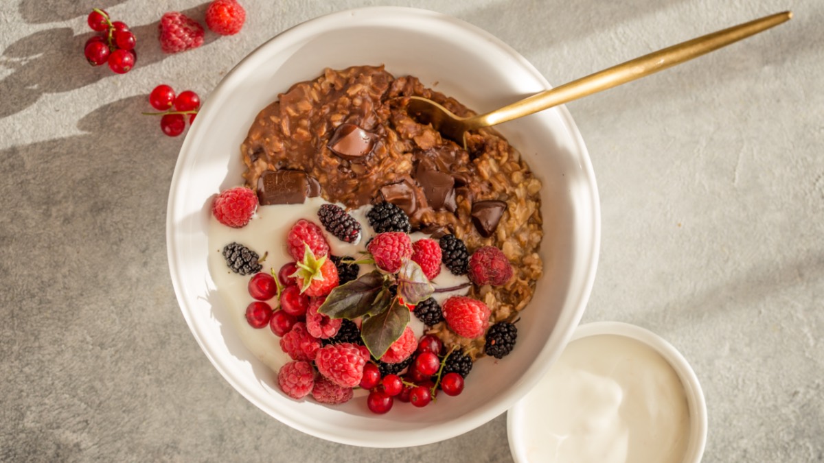 Schokoladen-Porridge in weißer Schüssel mit Obst, Draufsicht.