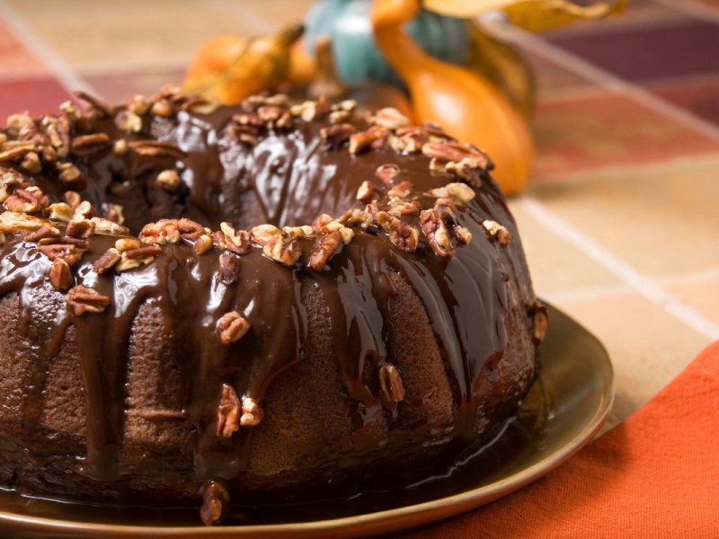Ein Schokoladenkuchen mit Kartoffelbrei auf einem Teller. Er ist mit Schokoladensoße und Nüssen garniert.