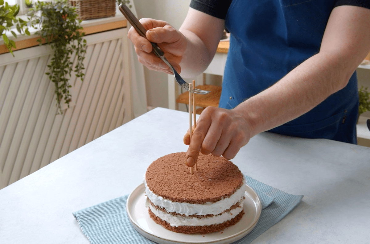Eine Gabel wird oben an zwei Holzstäben fixiert, die in der Schokoladentorte stecken.