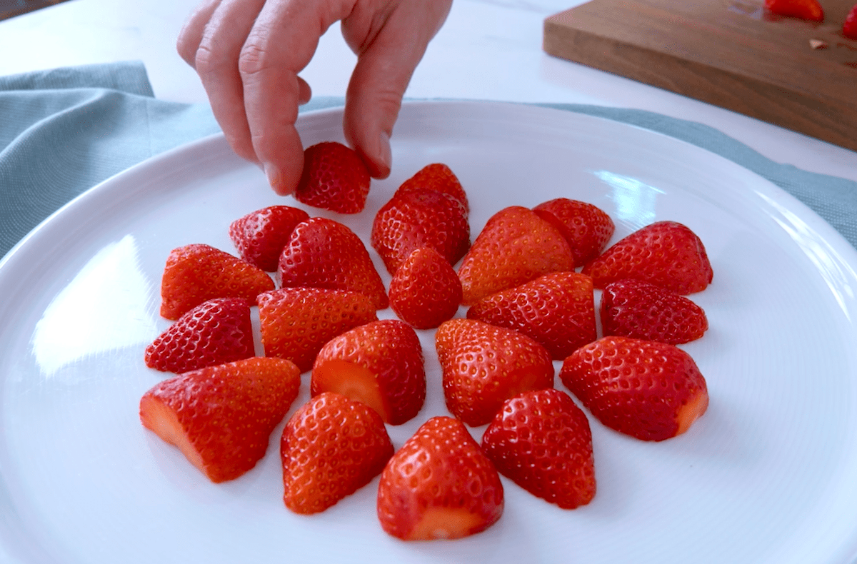 halbierte Erdbeeren werden mit der Schnittkante nach unten auf einem Teller gelegt