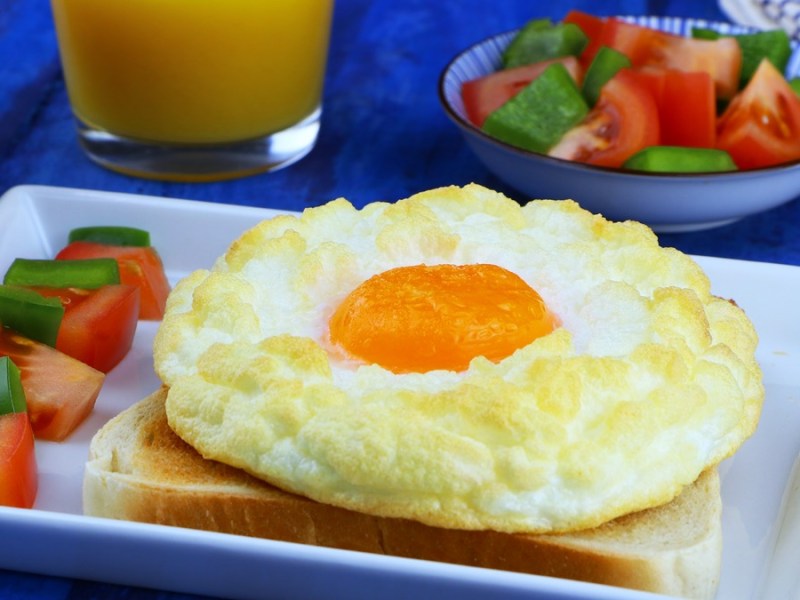 Ein fluffiges Wolkenei auf Toast mit aufgeschnittenen Tomaten auf einem Teller.