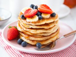 Ein Turm aus amerikanischen Pancakes, gestapelt auf einem Teller. Dekoriert mit Erdbeeren, Blaubeeren und Bananen.