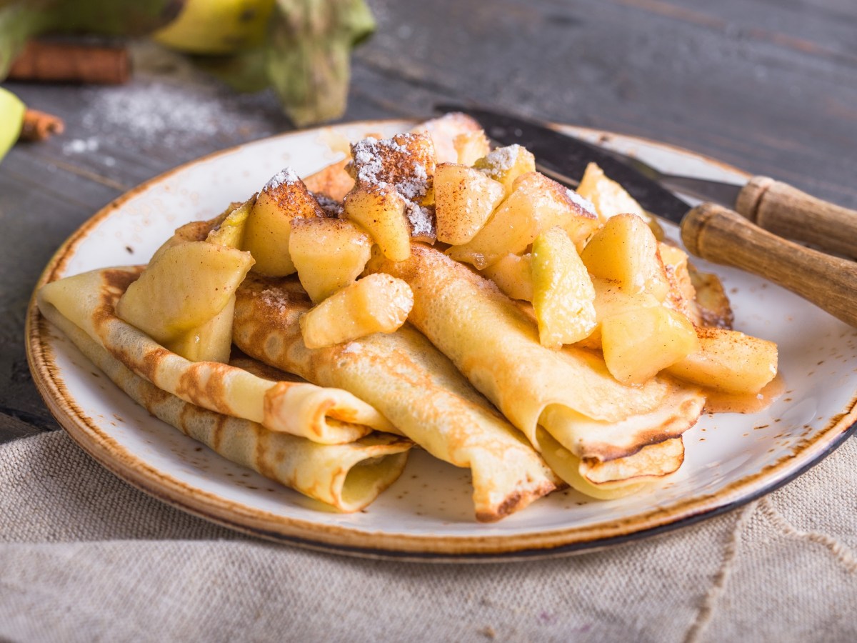 Ein Teller mit Bratapfel-Pfannkuchen, auf denen Apfelkompott liegt, daneben Messer und Gabel mit Holzgriffen.