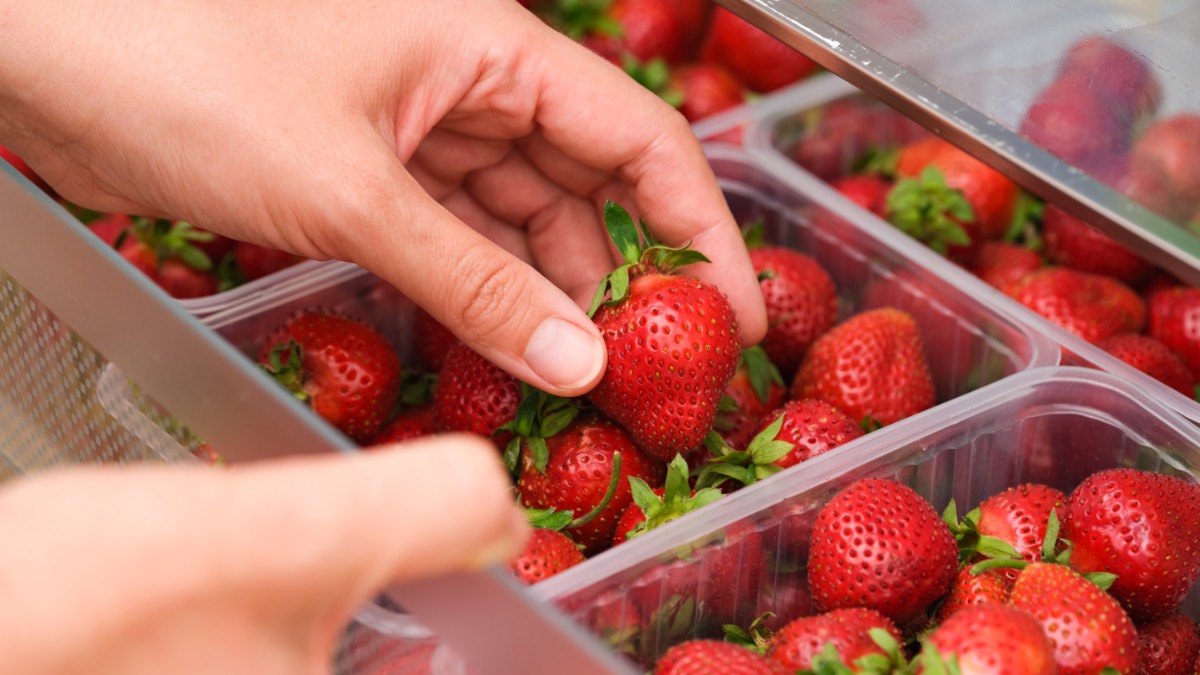 Eine Frau entnimmt eine Erdbeeren aus Plastikschale im KÃ¼hlschrank