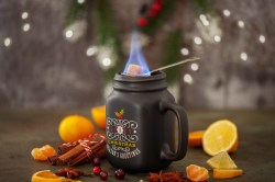 Eine Tasse Feuerzangenbowle mit weihnachtlicher Verzierung, darauf ein Löffel, auf dem ein Stück Zucker brennt.