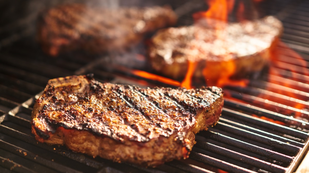 3 Scheiben Fleisch werden auf einem Grill gegrillt, aus dem Flammen nach oben schlagen