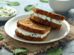 Zwei gegrillte Käse-Spinat-Sandwiches auf einem Teller, drumherum Babyspinatblätter und im Hintergrund unscharf eine Schüssel mit Frischkäsecreme.