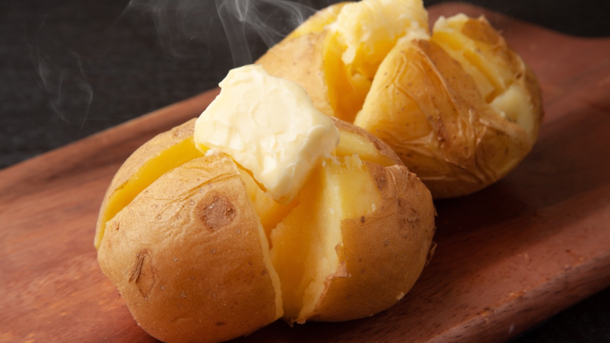 Zwei gekochte Kartoffeln mit Butter auf Holzbrett.