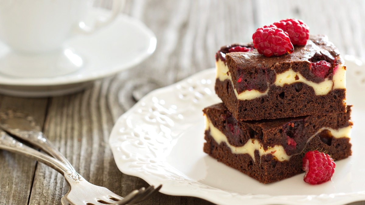Zwei Himbeer-Cheesecake-Brownies Ã¼bereinander gestapelt auf einem Teller mit frischen Himbeeren dekoriert