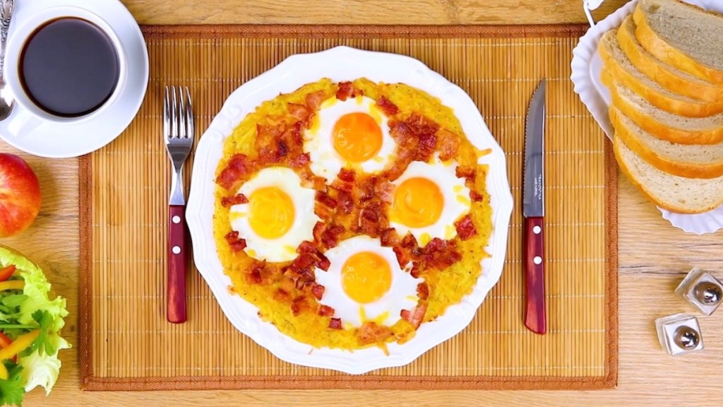 Ein Kartoffel-Rösti mit Ei, daneben eine Tasse Kaffee, Besteck und Brot.