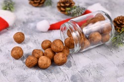 Ein umgekipptes Glas Marzipankartoffeln, drumherum Tannenzapfen und kleine Weihnachtsmützen.
