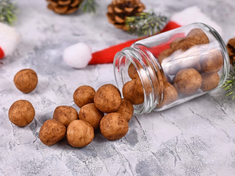 Ein umgekipptes Glas Marzipankartoffeln, drumherum Tannenzapfen und kleine Weihnachtsmützen.