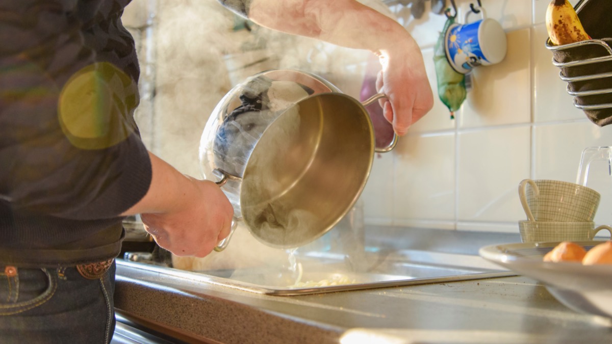 Mann gieÃŸt Nudeln in ein Sieb ab