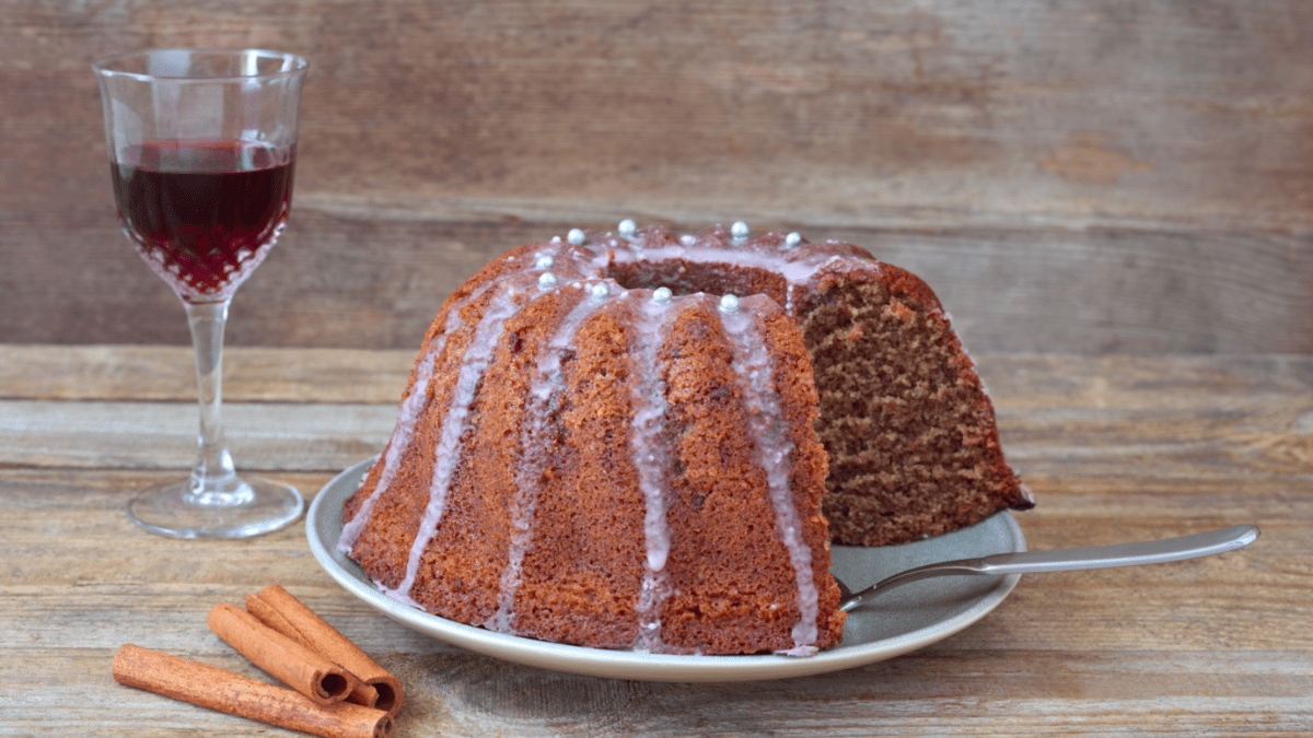 Angeschnittener Rotweinkuchen, daneben ein Glas Rotwein und einige Zimtstangen