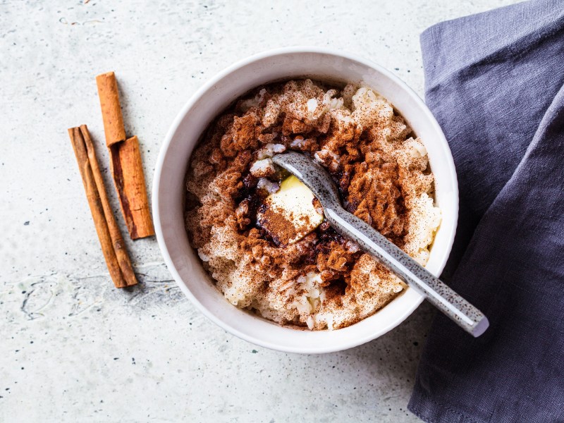 Eine Schüssel Spekulatius-Porridge mit einem Löffel, daneben Zimtstangen und eine blaue Serviette aus Stoff, alles Draufsicht.