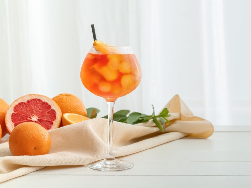 Ein Glas alkoholfreier Aperol Spritz mit Eiswürfeln und Orangenscheiben, daneben angeschnittene Zitrusfrüchte.
